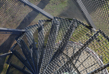 View down on narrow tight outdoor steep spiral steel staircase with steps made of metal lattice - Germany