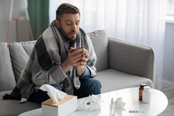 Man covered in blanket feeling sick, having hot drink