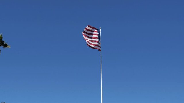 Driving by American Flag Waving on a Pole Between Buildings Under Clear Sky, POV of Right Seat Passenger in Moving Vehicle, Slow Motion