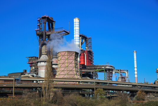 Duisburg (ruhrgebiet), Germany - March 1. 2021: View on industrial complex with smoking chimneys and tower against blue sky - Thyssen Krupp steel company