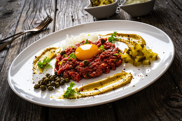 Beef tartare steak with onion, capers and pickled cucumbers on wooden table
