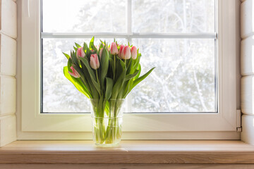 Bouquet of beautiful pink tulips on a wooden windowsill. White window in a Scandinavian style wooden house overlooking the garden, pine forest. Spring concept, Happy 8 March, Women's Day