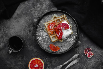 Belgian waffles with a bloody orange on a dark plate. Dark photo