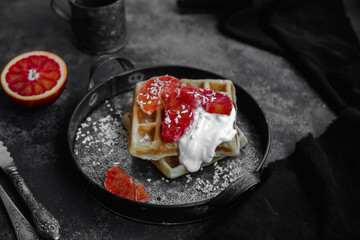 Belgian waffles with a bloody orange on a dark plate. Dark photo