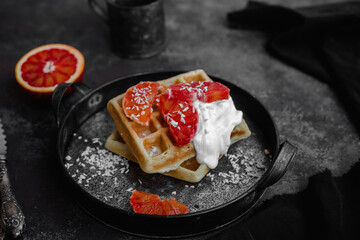Belgian waffles with a bloody orange on a dark plate. Dark photo