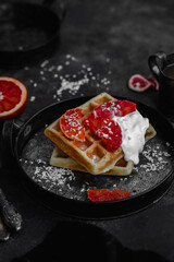 Belgian waffles with a bloody orange on a dark plate. Dark photo