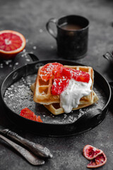 Belgian waffles with a bloody orange on a dark plate. Dark photo