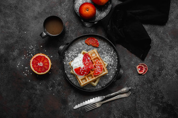 Belgian waffles with a bloody orange on a dark plate. Dark photo