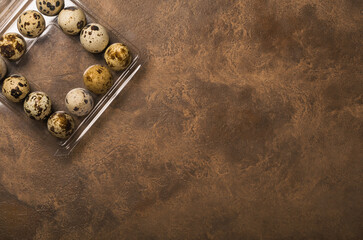 Many quail eggs in plastic packaging on brown background. Copy space.