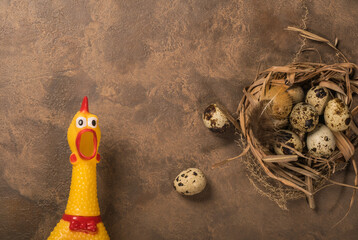 Yellow plastic chicken with quail eggs on a brown background