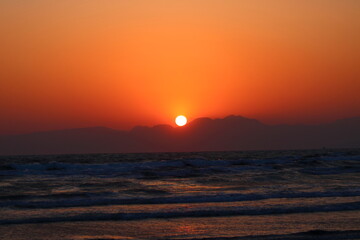 海岸線から臨む山あいに沈む夕日