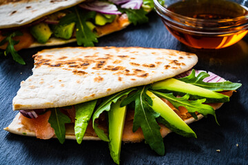 Italian piada wraps - piada stuffed with smoked salmon, avocado, arugula and onion on black stone plate 