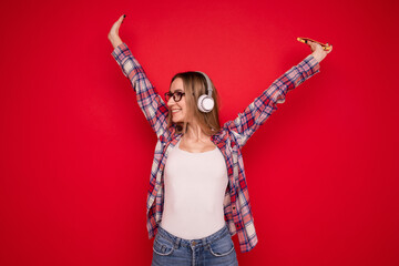 A happy young woman listens to music with headphones from her phone on a red background