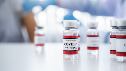 Covid-19 coronavirus vaccine bottles on white table with doctor injecting vaccine for middle aged woman background. Fight against Covid-19 coronavirus Concept.