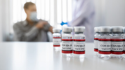 Covid-19 coronavirus vaccine bottles on white table with doctor injecting vaccine for old man background. Fight against Covid-19 coronavirus Concept.