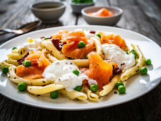 Maccheroni al ferretto with salmon nuggets, peas and sun-dried tomatoes on wooden table