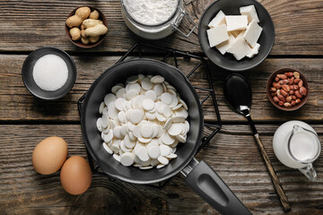 Saucepan with chocolate drops and ingredients for bakery on wooden background