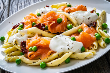 Maccheroni al ferretto with salmon nuggets, peas and sun-dried tomatoes on wooden table