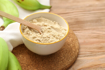 Bowl and spoon with banana flour on wooden background