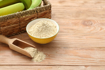 Bowl and scoop with banana flour on wooden background