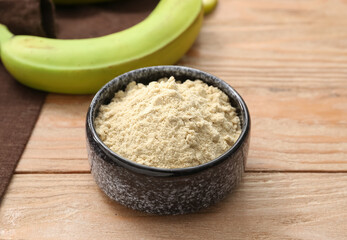 Bowl with banana flour on wooden background