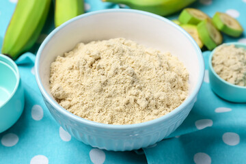Bowl with banana flour on fabric background