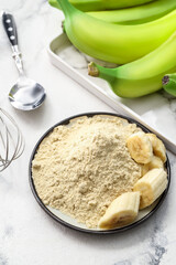 Plate with banana flour on light background