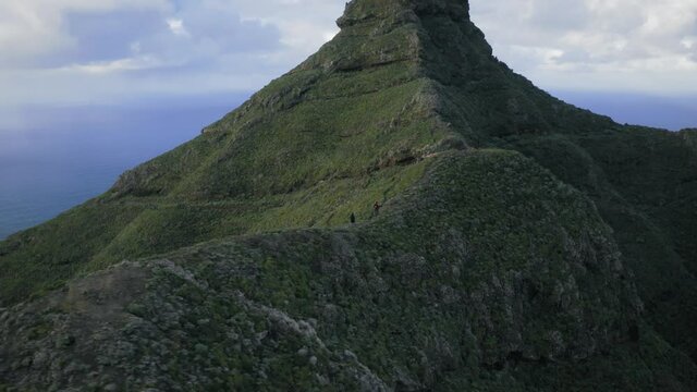 Aerial view of adventurous hikers walking towards their goal in Roque de Taborno in epic Tenerife island landscape near Atlantic ocean.