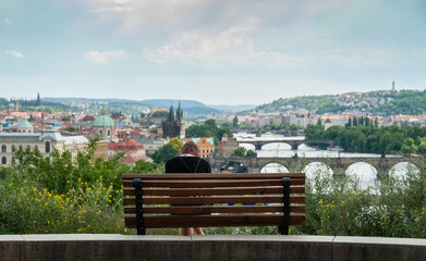A person sitting on a bench in Stalin lookout with a beautiful view of Prague, Moldau river and its bridges, Czech Republic