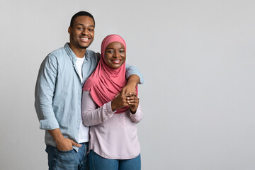 Cheerful loving african american muslim couple hugging on grey