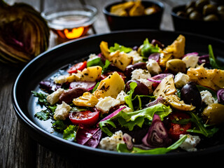 Fresh vegetable salad with feta cheese, artichokes, arugula, lettuce and cherry tomatoes on wooden table
