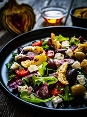 Fresh vegetable salad with feta cheese, artichokes, arugula, lettuce and cherry tomatoes on wooden table
