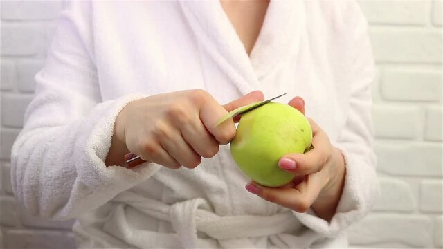 woman in bathrobe peeling a green apple close up