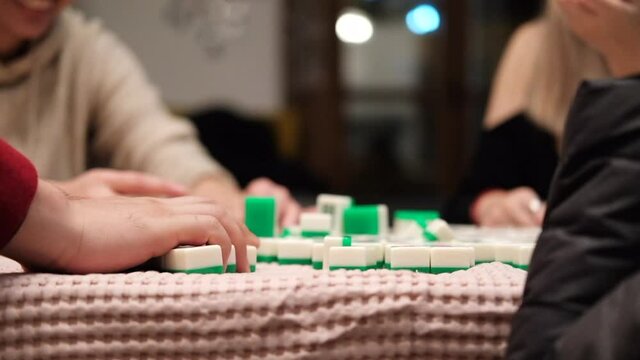 Friends playing mahjong at home in the evening on a red tablecloth