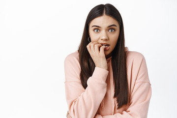 Excited young woman biting fingers and staring at camera with temptation and excitement, anticipating something, watching interesting moment, white background