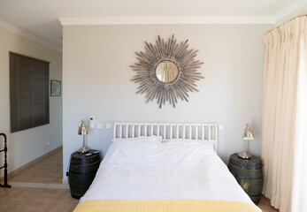 Simple bedroom with ornate sun mirror above a white double bed