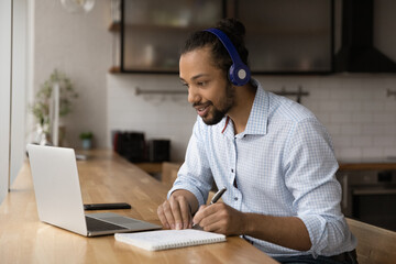 Close up motivated African American man wearing headphones watching webinar, writing taking notes,...
