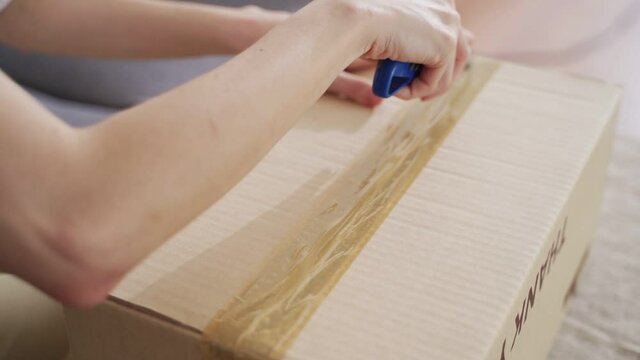 female hand using sharp cutter knife slashing tape on cardboard box to open carton parcel..