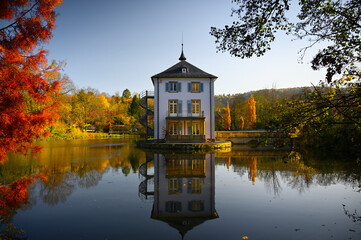 A baroque house, called Trappenseeschl&ouml;sschen, surrounded by Lake Trappensee in Heilbronn, Germany during autumn. The house and the colorful trees reflect in the water.