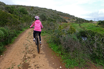 Naklejka premium Girl in pink jumper riding a mountain bike along a dirt track