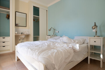 Fototapeta na wymiar Bedroom with unmade bed with white linen and blue wall