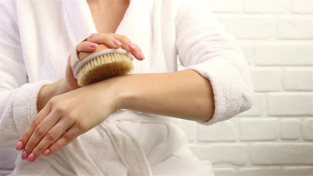woman in bathrobe massaging her arm with brush dry massage scene close up