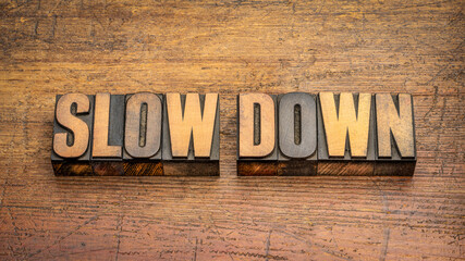slow down word abstract in vintage letterpress wood type against rustic wooden background, work, stress and lifestyle concept