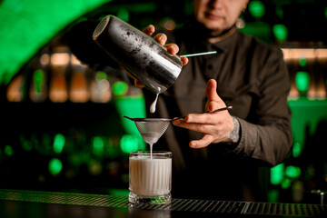 bartender accurate pours cocktail from shaker through sieve into old fashioned glass with ice