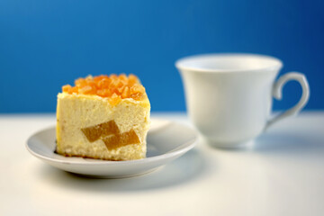 Mousse cake with marmalade on a white plate white cup on blue background