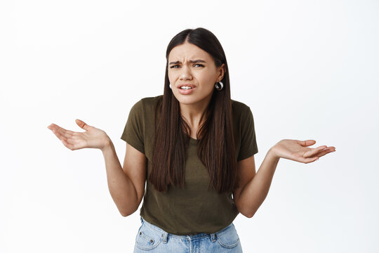 What I Dont Understand. Confused Brunette Woman Staring Puzzled At Camera, Shrugging And Spread Hands Sideways Clueless, Dont Know What Person Want, White Background