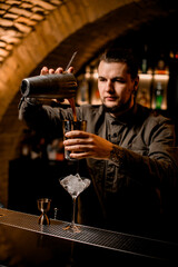 bartender carefully pours cocktail from one shaker cup to another