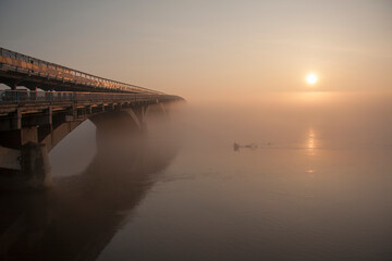 Sunrise over the spring river.  A bridge over a large river.. Fog on the river in early spring
