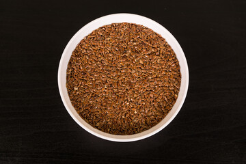 pile of Flax seeds in round white bowl on black table top view