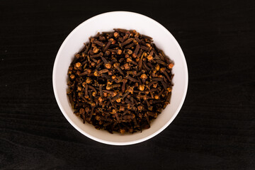 pile of cloves in round white bowl on black table top view
